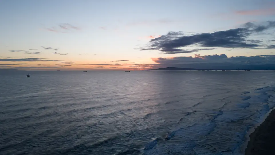 Aerial view of the calm Pacific Ocean at dusk with a pastel sky and ships on the horizon