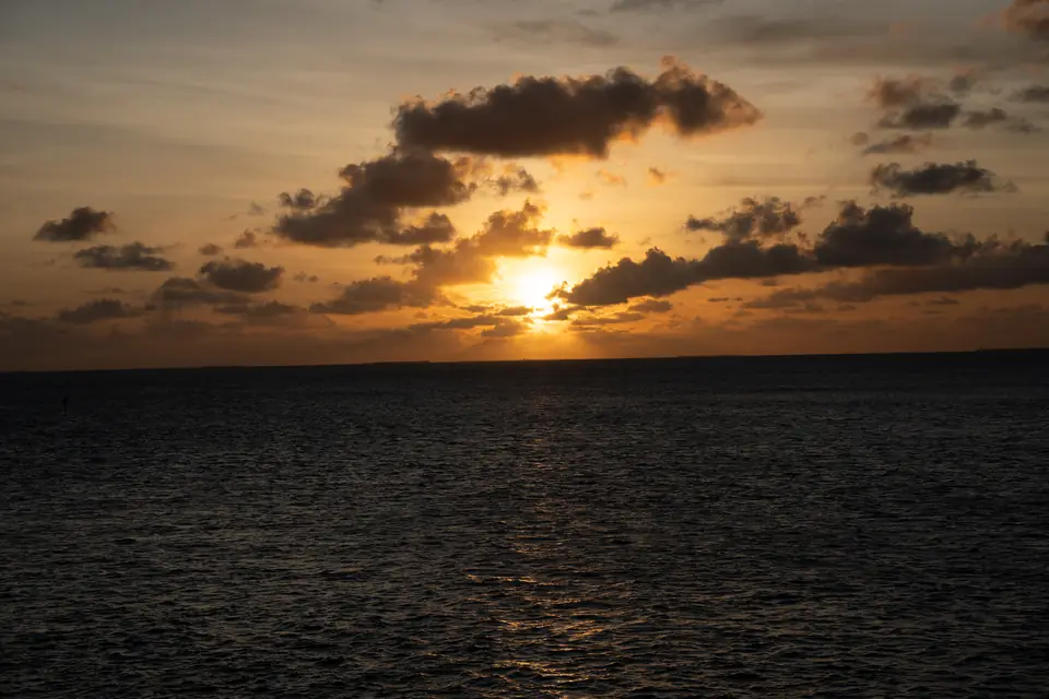 The setting sun bursting through clouds over open water