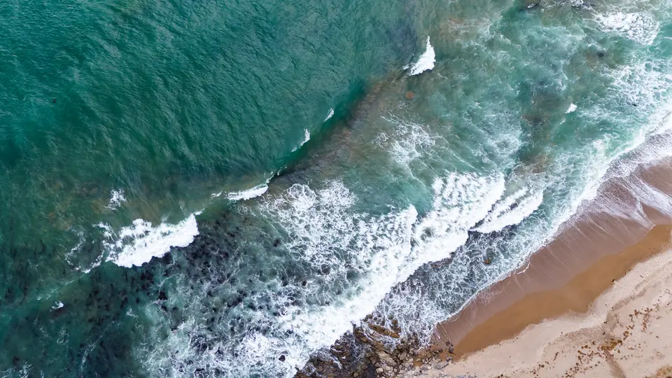 Top-down drone view of turquoise waves rolling onto a sandy beach